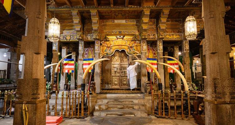 Interior of the ornate Temple of the Tooth with golden décor, carved pillars and white-robed attendant.