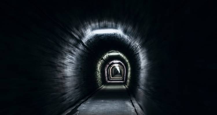 Schwach beleuchteter, enger Steintunnel mit dramatischer Fluchtpunktperspektive.