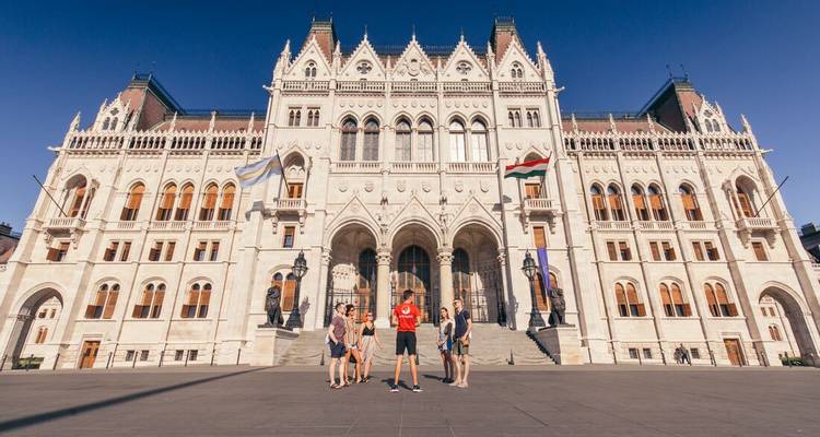 Touristen, die außerhalb des beeindruckenden neugotischen Ungarischen Parlamentsgebäudes in Budapest unter tiefblauem Himmel einem Führer zuhören.
