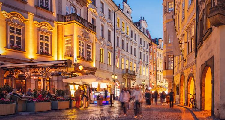 Abendliche Straßenszene in Prags Altstadt mit leuchtenden Cafélichtern und unscharfer Fußgängerbewegung.