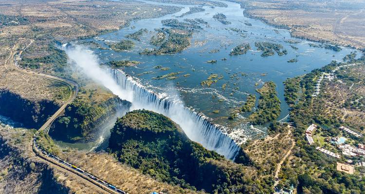 A dramatic aerial view of Victoria Falls with mist rising over the gorge and the Zambezi River winding beyond.