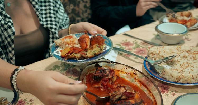 Hands serve plates of rice and richly sauced meat at a traditional Egyptian meal.