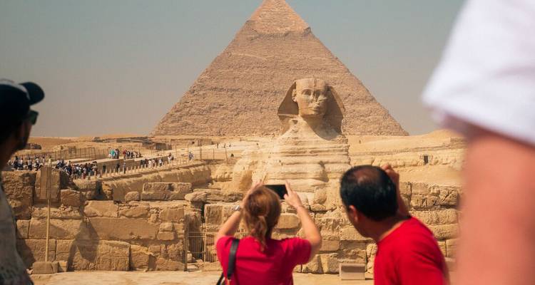 Tourists photograph the Great Sphinx with the Pyramid of Khafre rising behind it.
