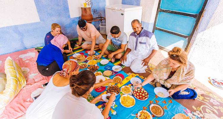 Local family and travelers share a colorful floor-spread meal in a bright courtyard.
