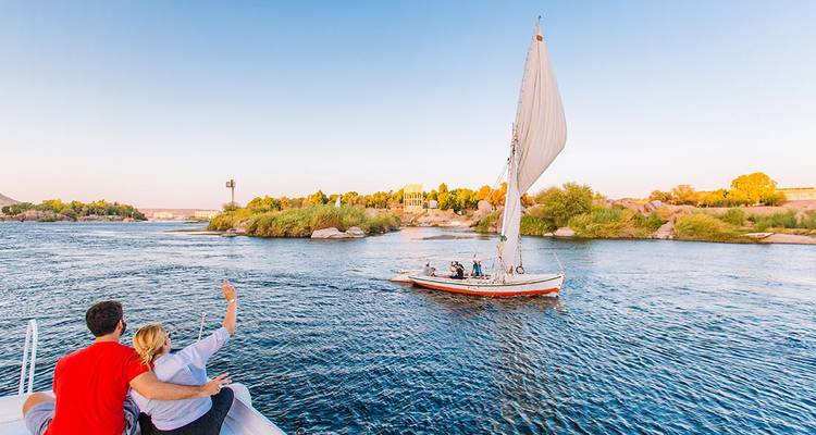 Couple on a boat wave at a traditional felucca sailing on the Nile at sunset light.