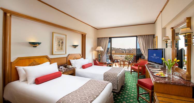 Bright, neatly appointed twin hotel room with balcony overlooking a cityscape.