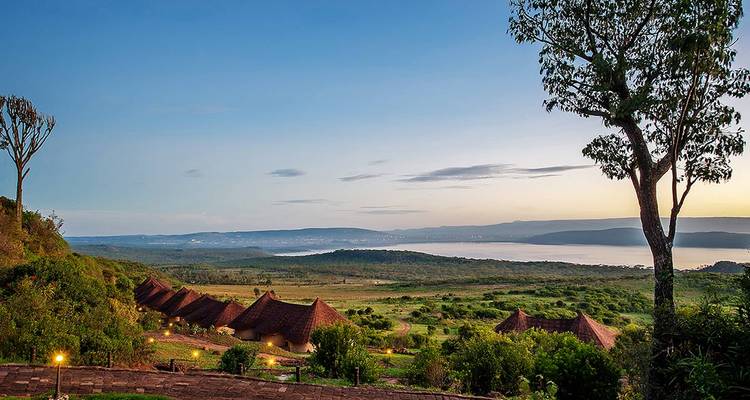 Panoramisch uitzicht vanaf een lodge op een heuvel met uitzicht op groene valleien en een glitterend Rift Valley-meer bij zonsopgang.