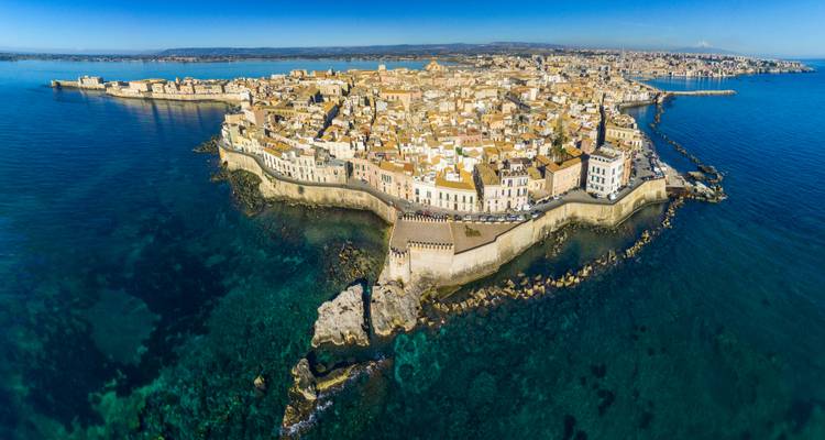 Vista de dron de la isla amurallada de Ortigia rodeada por un mar turquesa.