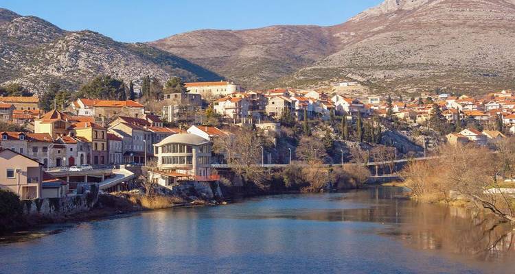 Riverfront town with orange rooftops nestled beneath rugged hills in southern Bosnia.