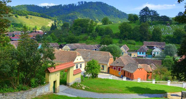 Picturesque Transylvanian village of pastel houses and rolling green hills under a clear sky.