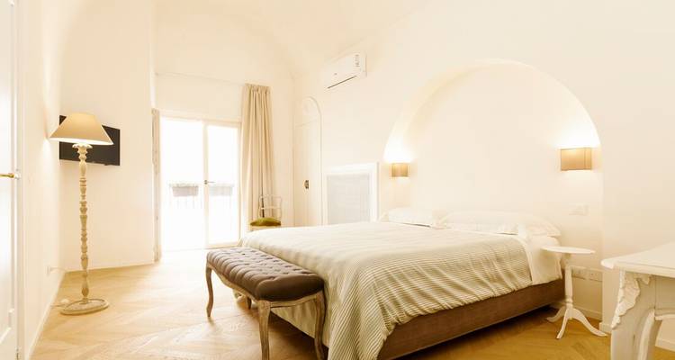 Chambre minimaliste lumineuse avec plafond voûté, grand lit et lumière naturelle douce.