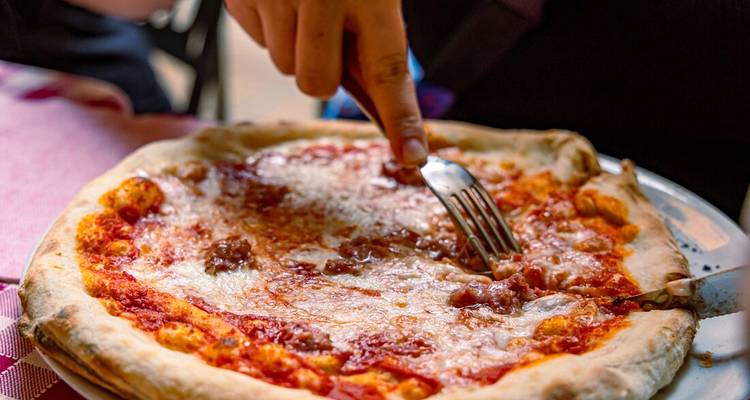 Gros plan d'une pizza margherita classique en train d'être coupée à la fourchette et au couteau.