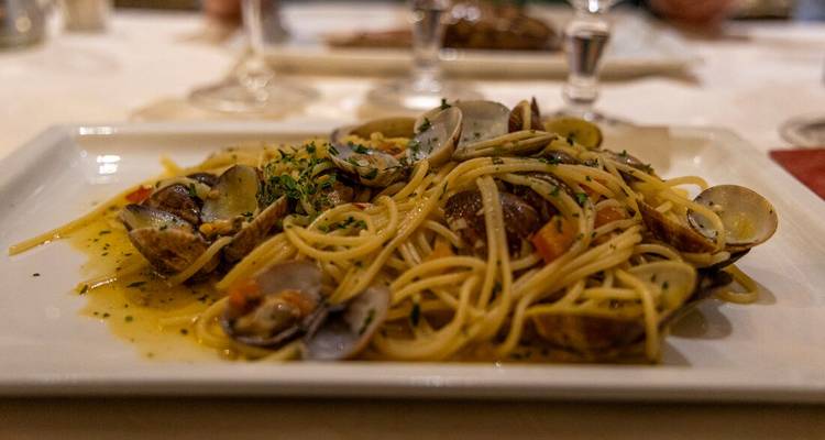 Assiette de spaghettis alle vongole garnie de palourdes et d'herbes aromatiques sur une table de restaurant.