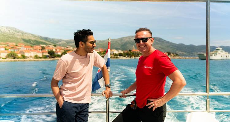 Two friends chat on the deck of a boat cruising turquoise waters past Croatian islands.