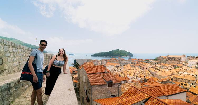 Travelers pose on Dubrovnik’s city walls with the terracotta rooftops and Adriatic in the background.
