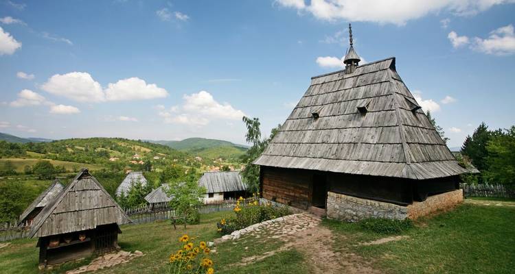 Rustic wooden cottages with steep shingled roofs in a serene rural Serbian landscape.
