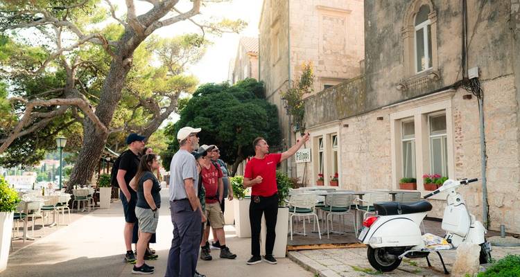 Guide in red shirt gestures while explaining architecture to a small tour group on a Croatian street.