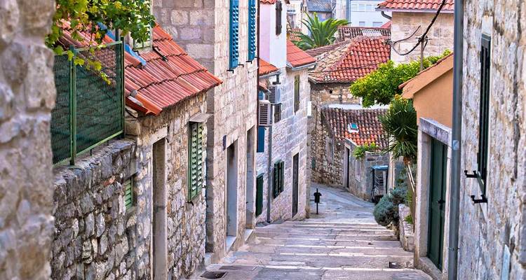 Narrow stone alleyway with terracotta rooftops and lush plants in a coastal Croatian town.