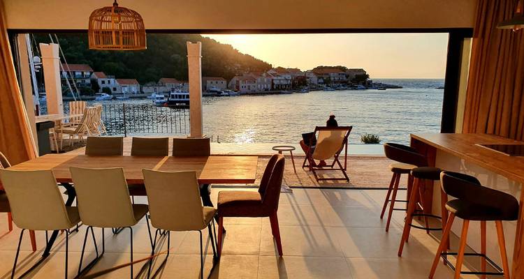 Open-plan dining room with wide glass wall framing a serene harbor view at sunset.