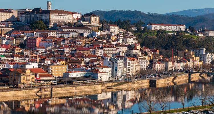 Vista urbana de Coimbra con techos de terracota reflejados en el río Mondego.