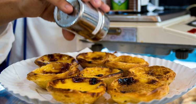 Des tartes à la crème portugaises fraîchement cuites saupoudrées de cannelle sur une assiette en papier au comptoir d'une boulangerie.