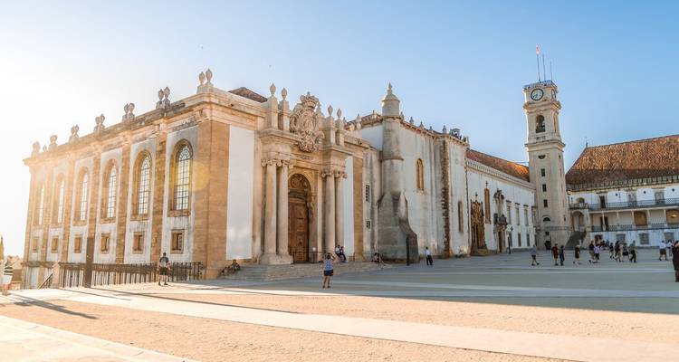 Les bâtiments baroques ensoleillés de la place de l'Université de Coimbra avec des visiteurs explorant l'esplanade spacieuse.