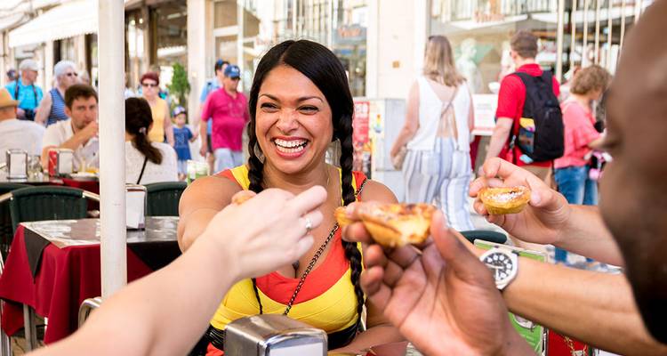 Des amis partagent une pâtisserie de nata à une terrasse de café en plein air à Lisbonne, souriants parmi les scènes animées de la rue.