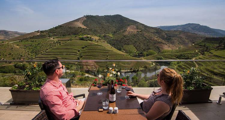 Un couple se détend avec du vin sur une terrasse surplombant les vignobles en terrasses de la vallée du Douro et le fleuve en contrebas.