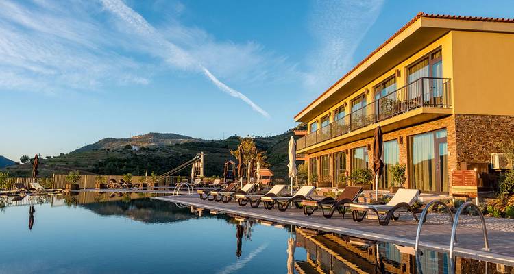 Lodge moderne situé à côté d'une piscine à débordement qui reflète les collines environnantes de la vallée du Douro sous une lumière chaude et douce du matin.