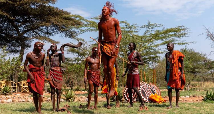 Des guerriers Maasaï effectuant une danse traditionnelle de saut en plein air parmi des acacias.