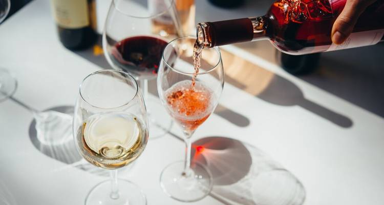Le vin rosé est versé dans des verres aux côtés de variétés blanches et rouges sur une table ensoleillée.