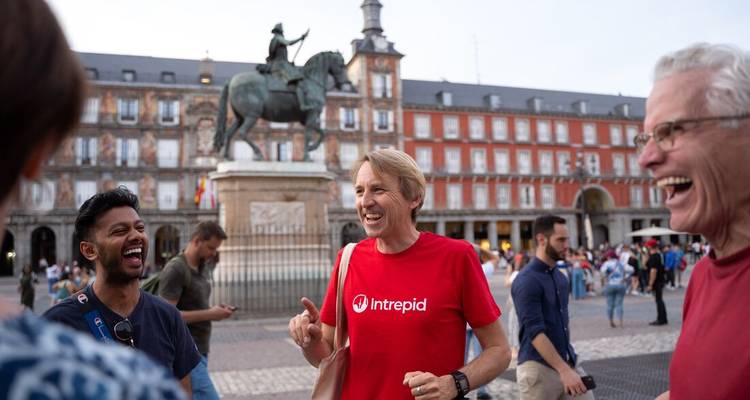 Des voyageurs souriants se rassemblent à la Plaza Mayor de Madrid avec la statue équestre derrière eux.