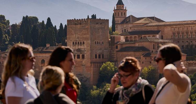 Les touristes discutent tandis que l'Alhambra majestueux se dresse de l'autre côté de la vallée dans la douce lumière du matin.