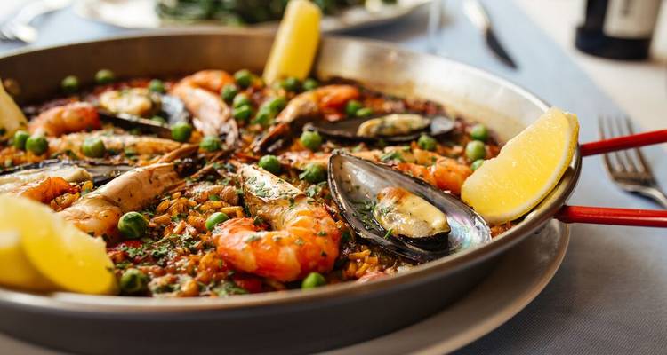 Gros plan d'une paella aux fruits de mer fumante garnie de quartiers de citron.