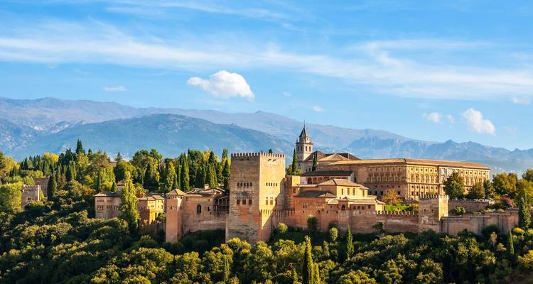 Vue panoramique de carte postale du complexe de l'Alhambra se détachant sur les montagnes de la Sierra Nevada et le ciel bleu.