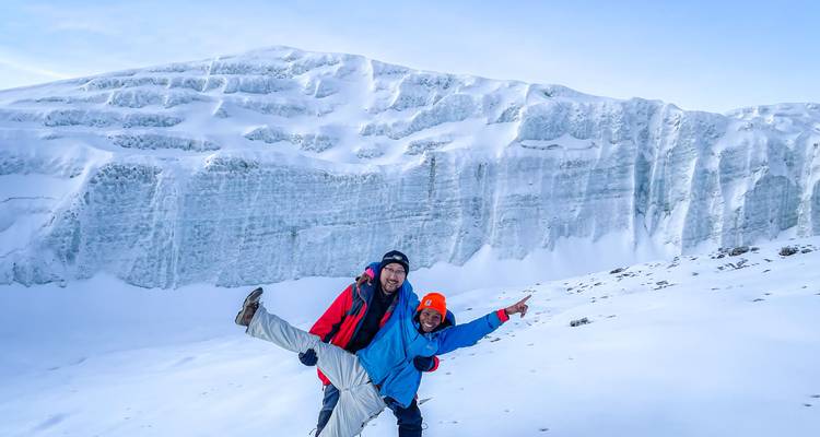 Two climbers celebrate before towering ice walls of Kilimanjaro’s glacier near the summit.