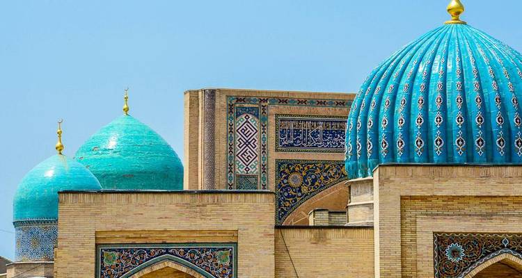 Turquoise tiled domes and ornate brickwork of an Uzbek mosque rise against a clear blue sky.