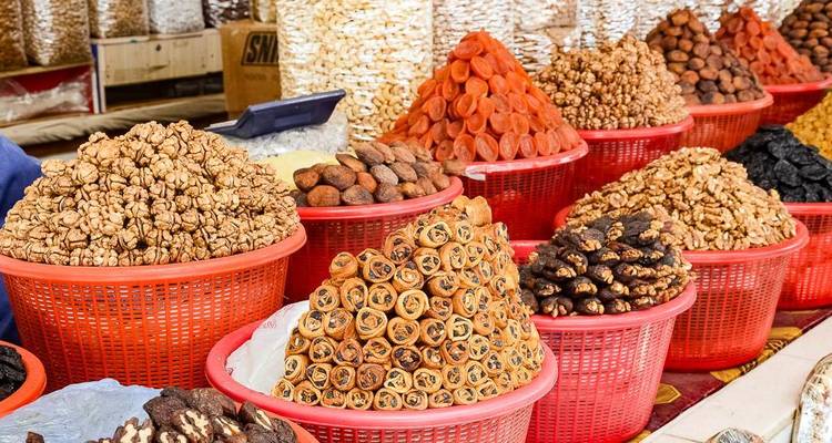 Rows of red baskets overflow with dried nuts and fruits in a vibrant Uzbek bazaar.