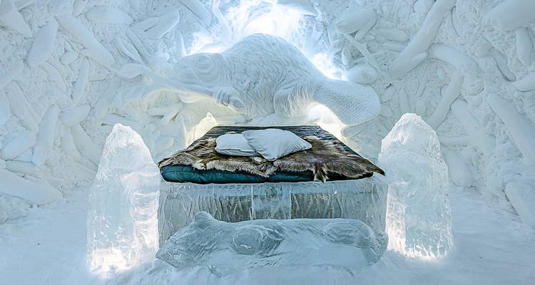 Une chambre d'hôtel de glace aux sculptures complexes présente un relief animal luminescent au-dessus d'un lit de glace recouvert de fourrure.