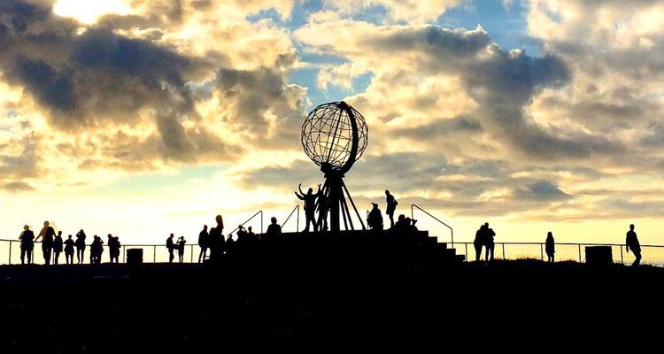 Des visiteurs en silhouette se rassemblent autour du monument globe iconique de Nordkapp sur un ciel de coucher de soleil dramatique.