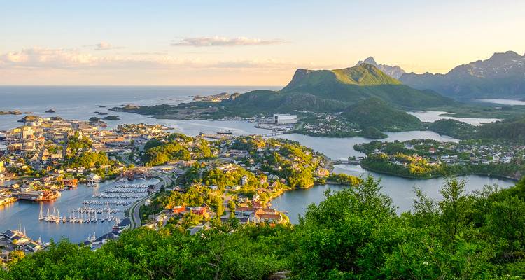Vue panoramique aérienne d'une ville côtière avec des marinas, des îles et des montagnes verdoyantes environnantes à l'heure dorée.