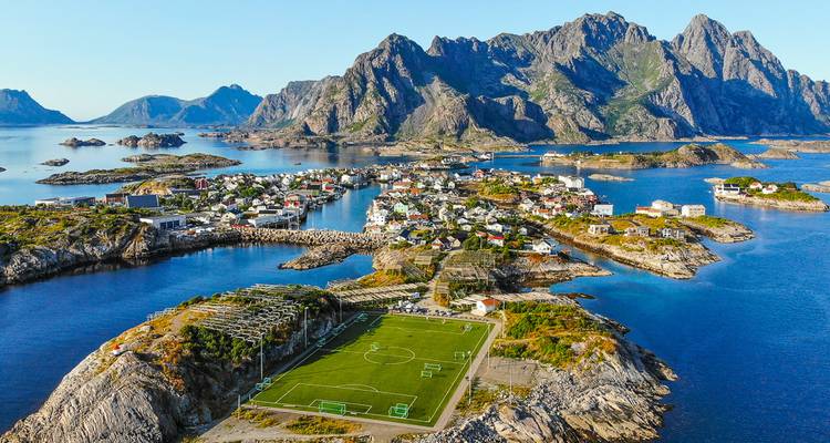 Vue aérienne des îles de Henningsvær présentant un terrain de football distinctif entouré d'une eau turquoise et de pics rocheux dentelés.