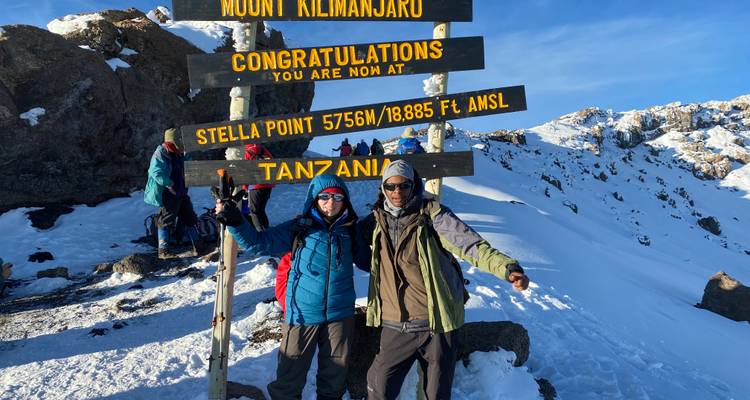 Deux randonneurs souriants se tiennent à côté du panneau Stella Point sur la crête du sommet enneigé du Mont Kilimandjaro.