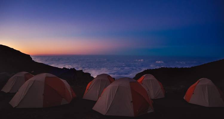 Des rangées de tentes dômes sur un site de camping en montagne au-dessus d'une mer de nuages à l'aube.