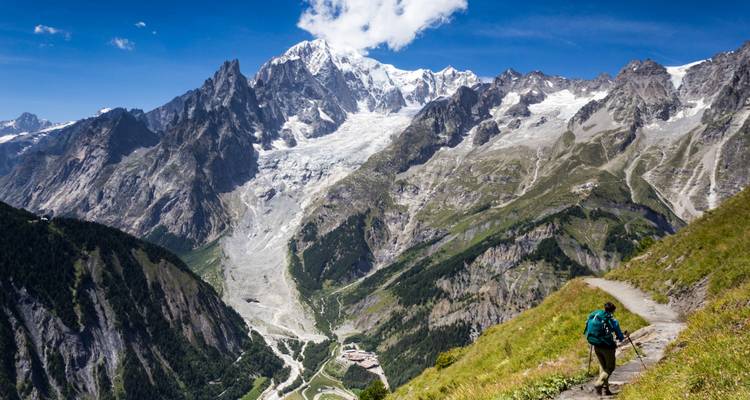 Trekker klimt over smal bergpad met de uitgestrekte gletsjers van Mont Blanc die dreigend voor hem uitrijzen.