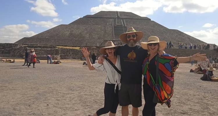 Drei lächelnde Reisende posieren mit erhobenen Armen vor der Pyramide der Sonne in Teotihuacan.