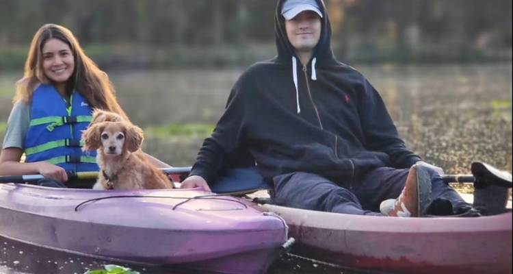 Un jeune couple avec un petit chien se détend dans des kayaks en tandem sur un lac calme au coucher du soleil.