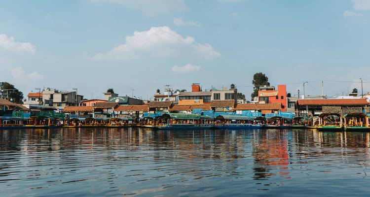 Rangée de bateaux trajinera aux couleurs vives le long des canaux de Xochimilco avec des reflets dans l'eau.