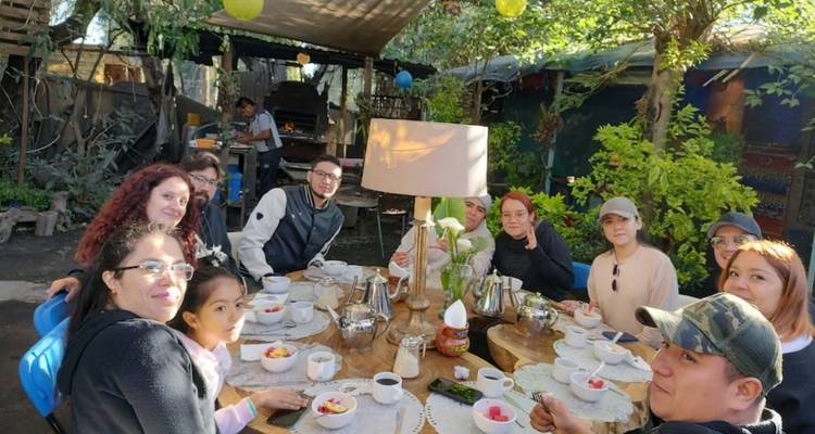 Un grand petit-déjeuner en famille rassemblé autour d'une table en bois rustique dressée en plein air sous les arbres.