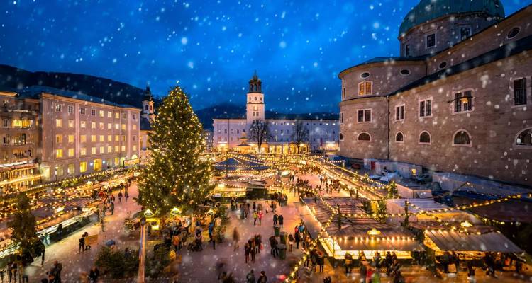 Marché de Noël de Salzbourg saupoudré de neige, illuminé par des lumières festives autour d'un grand sapin la nuit.
